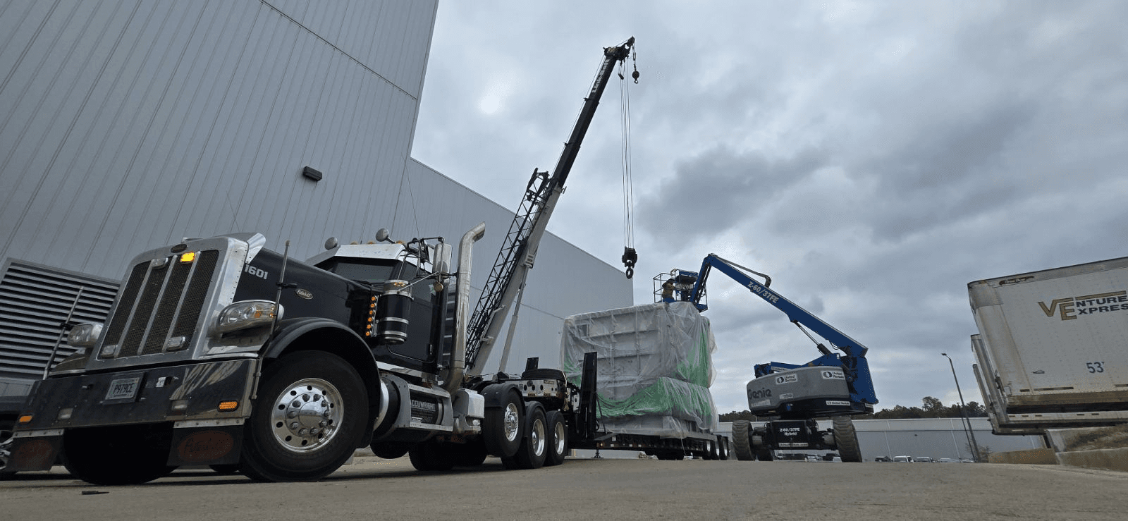 Industrial machinery delivery supported by a boom truck and lift equipment at a manufacturing facility