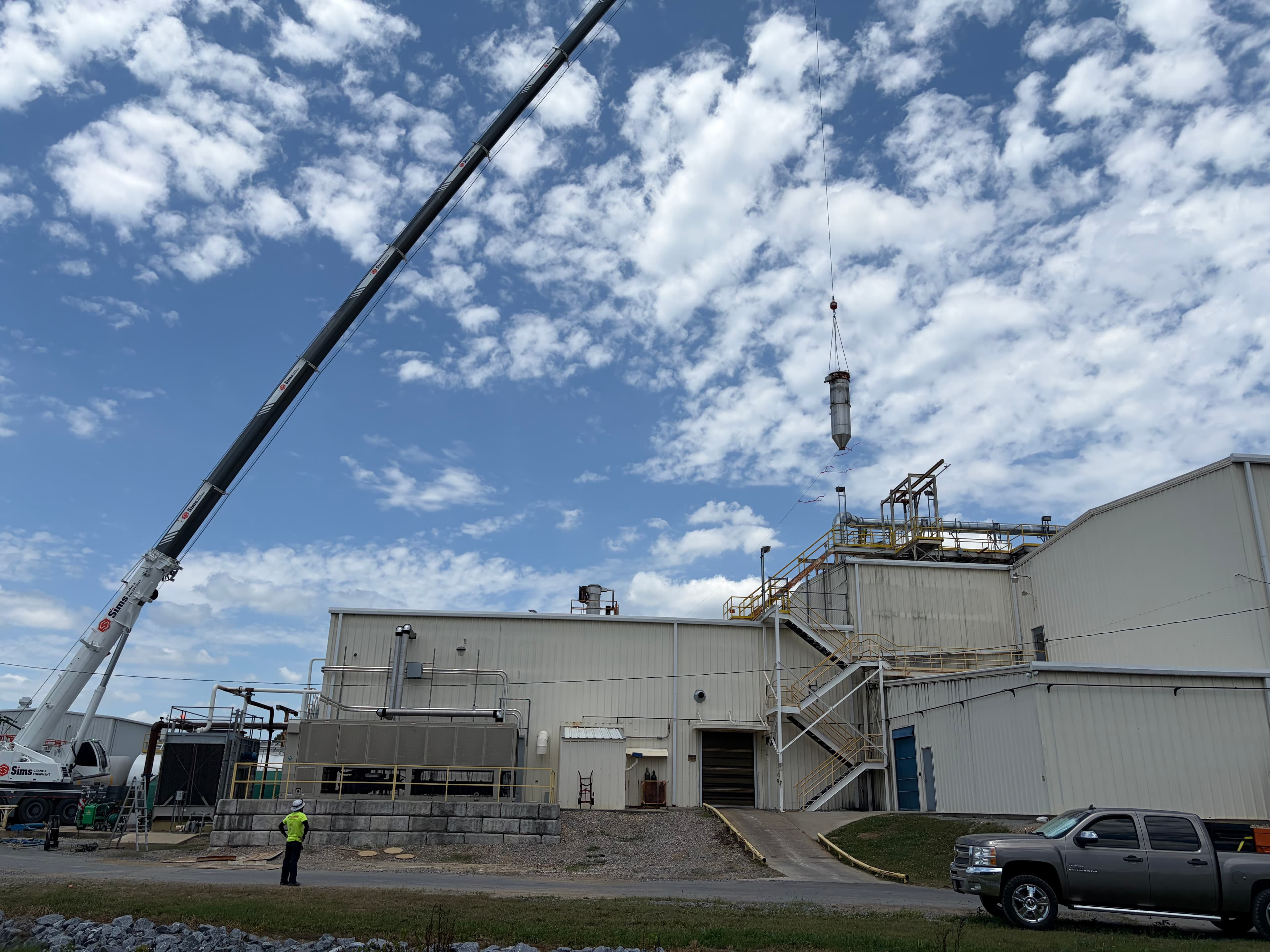 Mobile crane lifting industrial equipment above a manufacturing plant roof