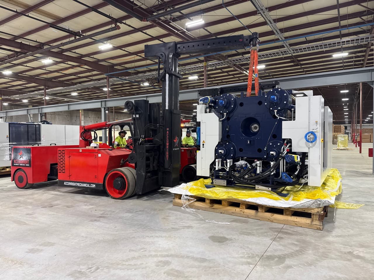 Industrial machinery rigging and heavy forklift installation Accuwright machinery riggers using a heavy forklift and boom attachment to install industrial equipment inside a manufacturing plant
